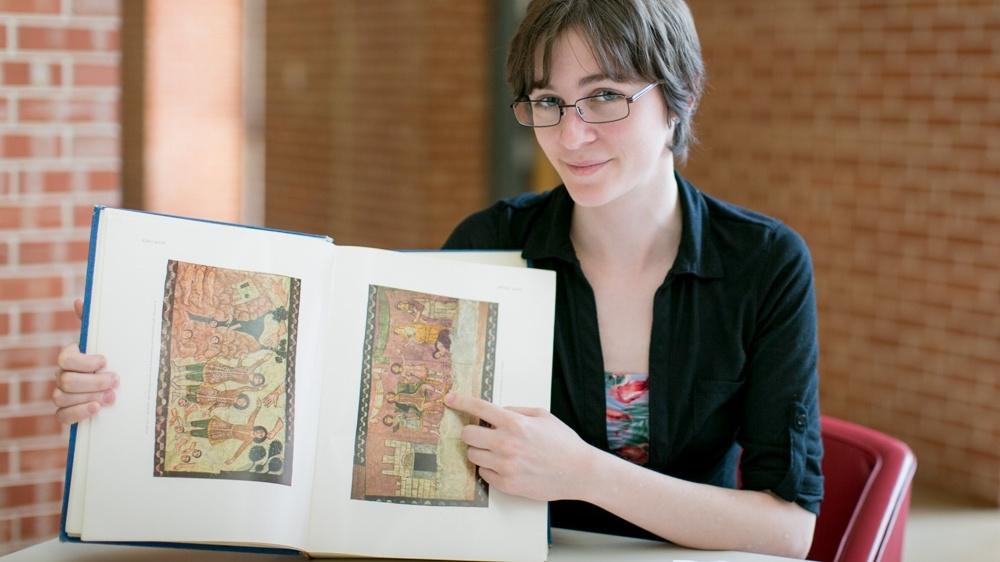 A student displays a book with ancient art